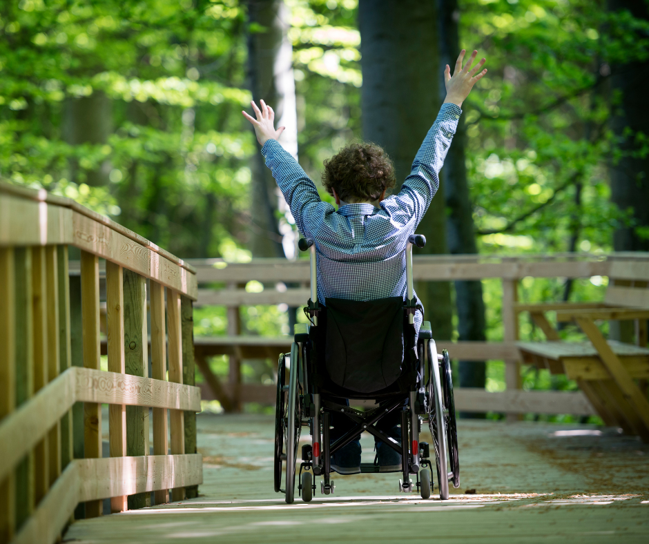 Person on a Wheelchair on a boardwalk in a park with trees in the background
